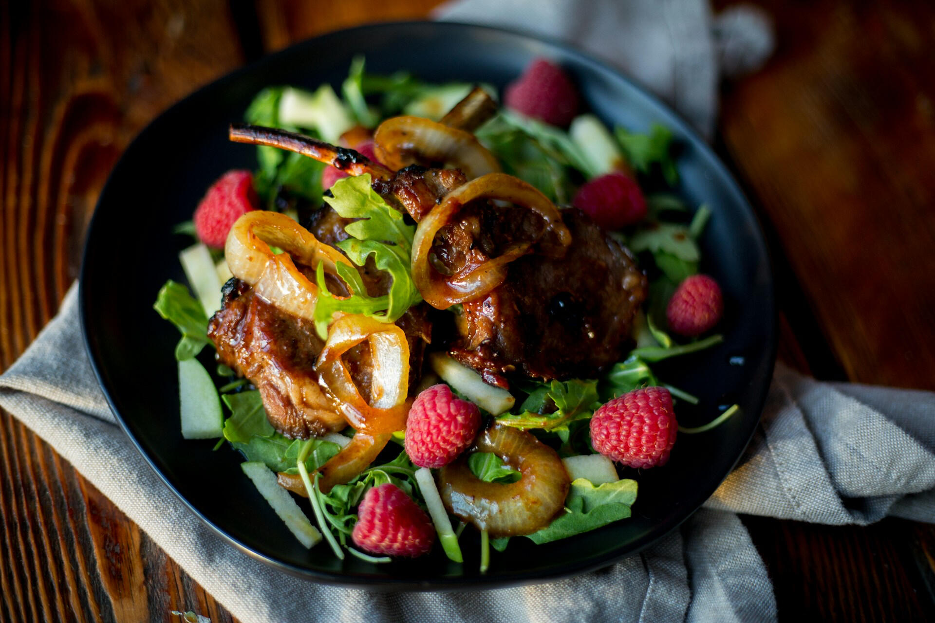 Tallrik med lammkött och en sallad med grönsaker och hallon